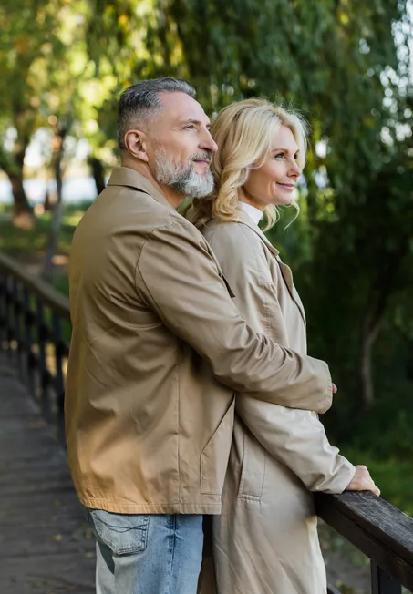 Pareja de personas mayores abrazadas contemplando el paisaje desde un puente de madera