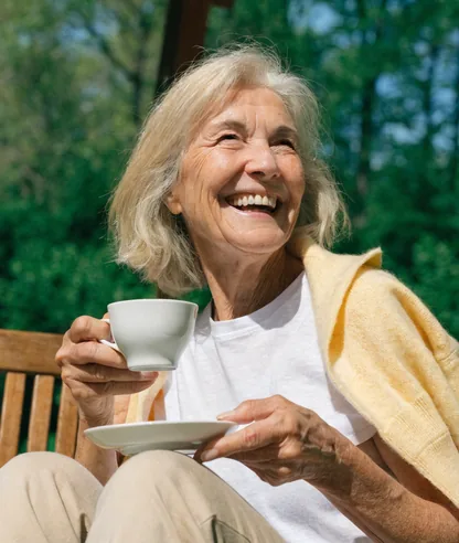 Mujer mayor sonriente tomando un café al sol en el jardín