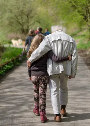 Hombre mayor caminando abrazado a una niña por un sendero arbolado